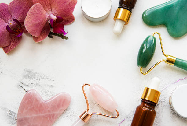 istock Face massage jade roller with cosmetic product on white marble background 1297330722