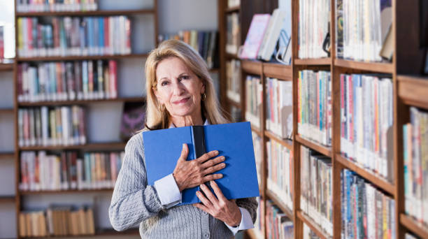 istock Senior woman reading book in library 1297334453