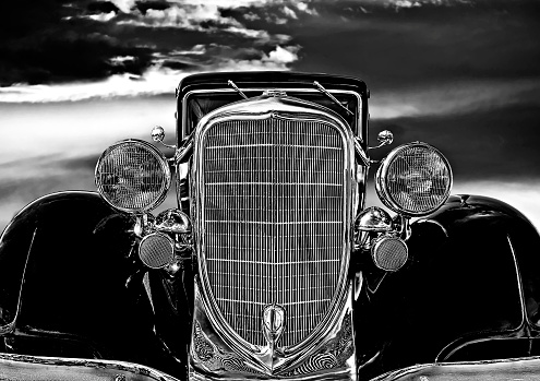 close view front of car foreground, background moody sky, no people, partial view of car, close up chrome grill