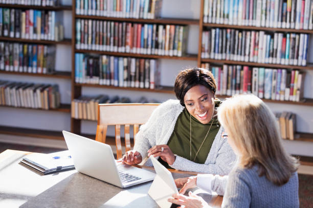 istock Two women with laptops working together in library 1297334463
