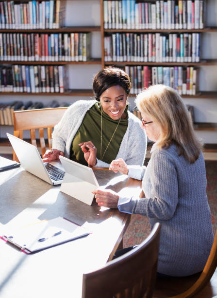 Two women with laptops working together in library
