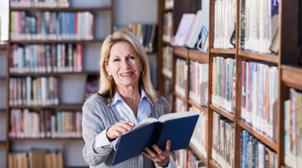 istock Senior woman reading book in library 1297334486