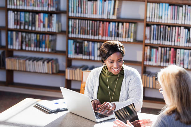 istock Two women with laptops working together in library 1297334495