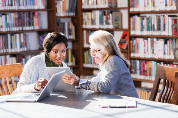istock Two women with laptops working together in library 1297334518