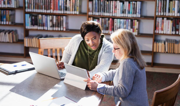 istock Two women with laptops working together in library 1297334524