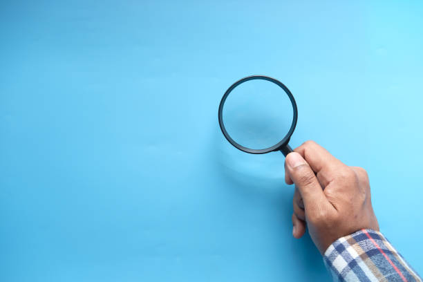 istock hand holding magnifying glass on blue background 1297340616
