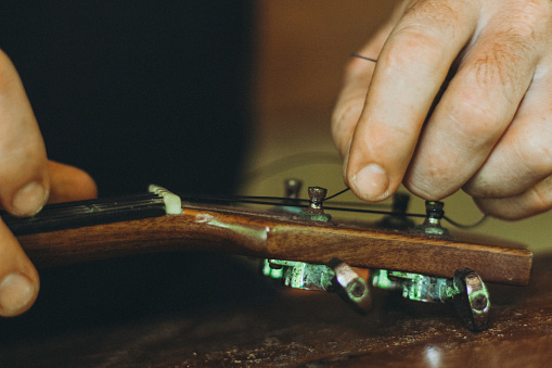 Tuning the string of ukelele, human hands, closeup. Process of changing string of ukulele