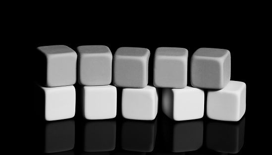 A pyramid of white and dark cubes on a black surface with a reflection. Close-up, isolated background, selective focus.