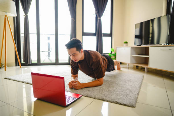 istock Young Asian man using laptop to learn plank position at living room 1297348255
