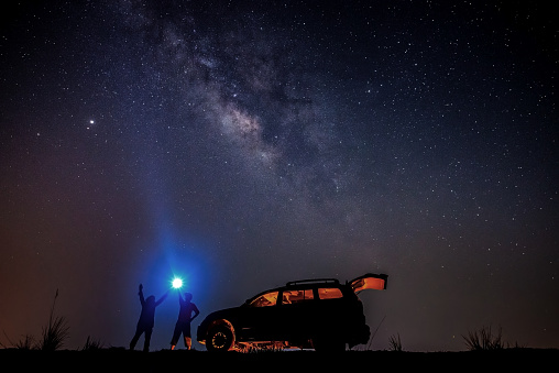 Man tourist with flashlight near his camp car at night. Space background with noise and grain. Night landscape with car and colorful bright milky way.Beautiful scene with universe.