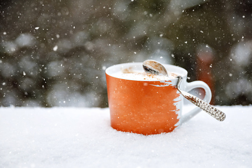 Fresh coffee in a cup in snow. Steaming beverage, coffee with milk or latte macciatto, capuccion or chocolate