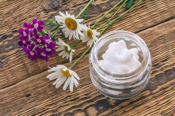 Cosmetic cream, fresh chamomile and verbena flowers on wooden background. Cosmetic cream in a glass jar, bouquet of verbena and chamomile flowers on old wooden boards. Top view. regenerative face cream stock pictures, royalty-free photos & images