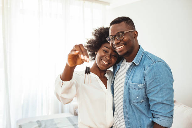 Young man surprising his wife or a girl with new a apartment. Happy young family couple holding key to new home on moving day concept, first time real estate owners man husband embrace woman wife look at camera proud buying property stand in own flat with boxes computer key stock pictures, royalty-free photos & images