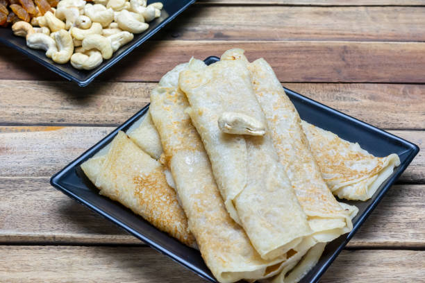 dolce bengalese - patishapta pitha in un piatto nero su sfondo di legno, una ricetta tradizionale di pancake bengalese dove i pancake sono ripieni di kheer o cocco. - cereal plant processed grains rice wheat foto e immagini stock