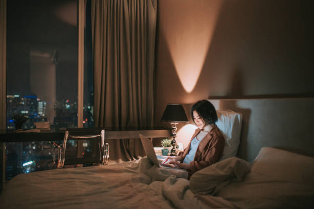 asiatico cinese bella donna che usa laptop lavorando da casa in camera da letto di notte - hotel wireless technology bedroom hotel room foto e immagini stock