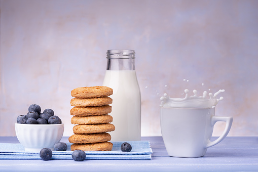 on lavender blue table, breakfast food with wholemeal shortbread cookies, blueberries and fresh milk with splash