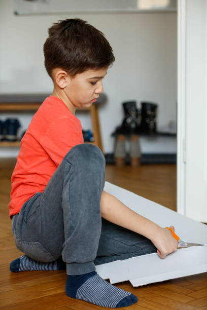 istock Boy sitting on the floor and cutting white cardboard with scissors 1297369198