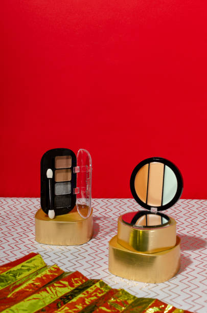 istock Concealer, eyeshaows on the decorative golden podiums, decorative shiny element on the grey surface against red background 1297369712