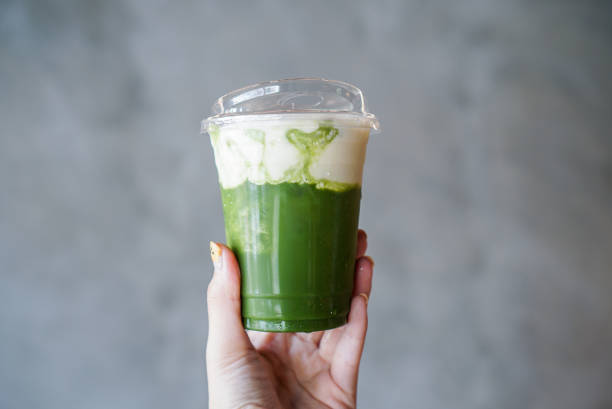 Hand holding a plastic cup of matcha green tea topped with milk cream.