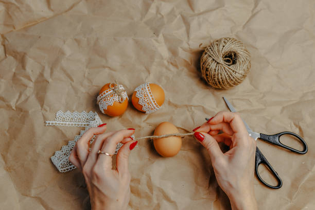 istock Decorating easter eggs on kraft paper with lace and rope. Three easter eggs on kraft paper background. Woman binding rope around the egg. 1297371818