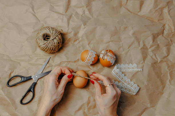 istock Decorating easter eggs on kraft paper with lace and rope. Three easter eggs on kraft paper background. Woman binding rope around the egg. 1297371825