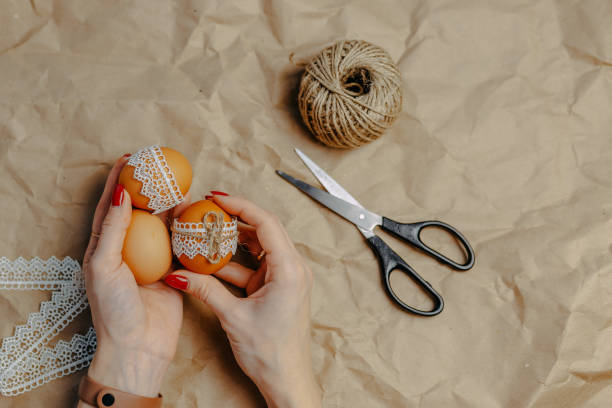 istock Decorating easter eggs on kraft paper with lace and rope. Three easter eggs on crumpled kraft paper background. Woman holds eggs in hands. 1297371826