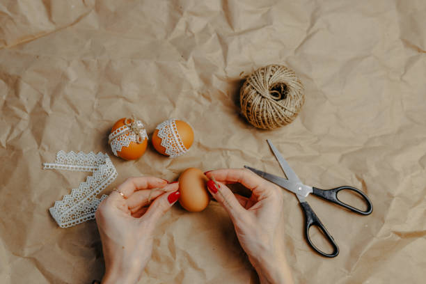 istock Decorating easter eggs on kraft paper with lace and rope. Three easter eggs on kraft paper background. Woman binding rope around the egg. 1297371828