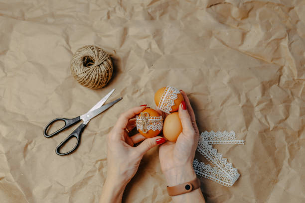 istock Decorating easter eggs on kraft paper with lace and rope. Three easter eggs on crumpled kraft paper background. Woman holds eggs in hands. 1297371834