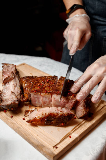 istock Waiter with gloves cuts Tomahawk steak on a beef bone into pieces for restaurant guests. Close-up of hands 1297372471