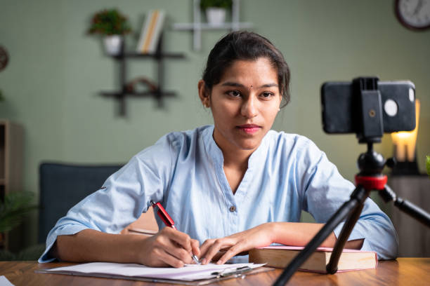 istock Young college girl student writing notes by looking into mobile phone during online Class - concept of new normal, virtual learning, online education during coronavirus or covid-19 pandemic. 1297372604