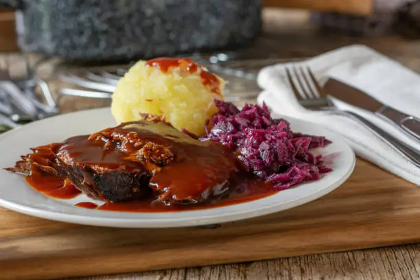 fresh cooked german sunday lunch dish with roast beef and delicious gravy, potatoe dumpling and red cabbage vegetable served on a plate with knife and fork