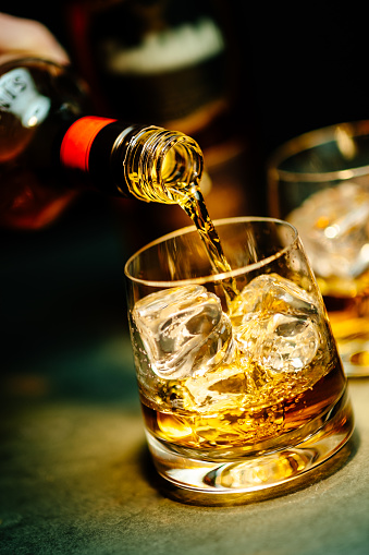 Pouring a glass of whiskey with ice, in a dark background.