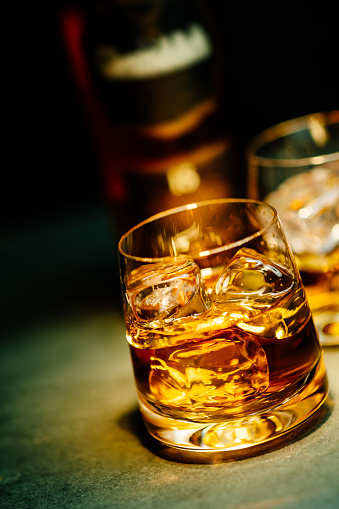 Glass of whiskey with ice and a square decanter isolated on a black background