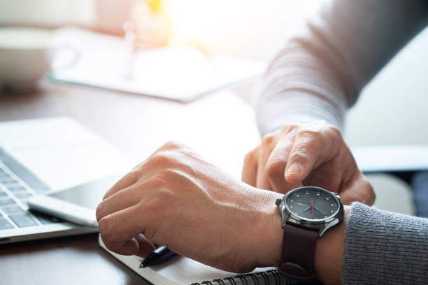 image de plan rapproché de montre brune de luxe de mode sur le poignet de l’homme. homme d’affaires travaillant avec l’ordinateur portatif sur le bureau de bureau. regarder et vérifier l’heure sur sa montre-bracelet, une horloge sur ses mains. - vérifier lheure photos et images de collection