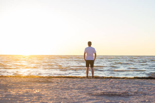 istock A man in a white shirt and brown shorts standing on empty beach at sunrise. 1297380697