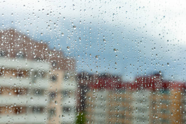 istock Close up of a window with rain drops falling down. Focus on rain drops. Rain drops on rainy day on outside window glass with blurred edges. Rain outside window pane in spring day. 1297382047