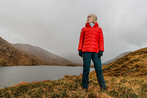 Mature woman wearing a red padded jacket on a cloudy winter's day at Loch Arkaig in the Highlands of Scotland.