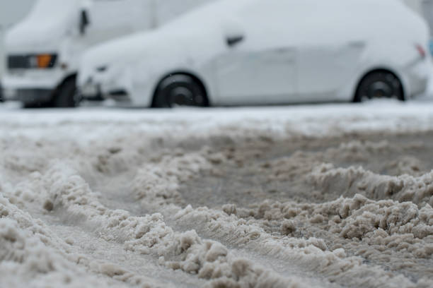 schmutziger eisiger schnee auf unreinigender stadtstraße gegen parkplatz - snow park road cold stock-fotos und bilder