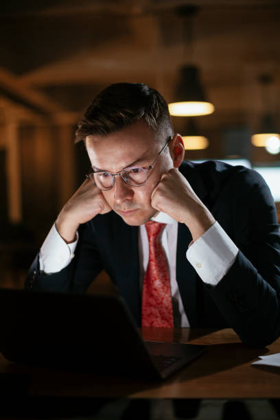 istock Tired man sitting at office desk working on laptop computer 1297383125