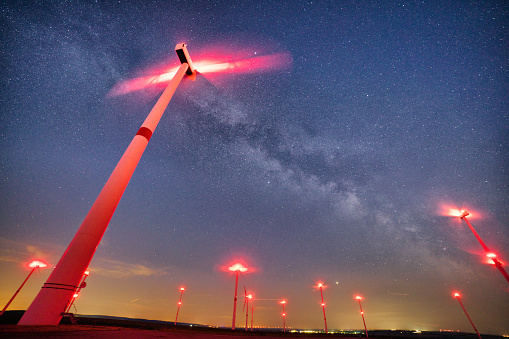 Looking up at wind turbines produces green energy under beautiful bright stars from our Milkyway galaxy. They represent an alternative energy solution and produce clean energy.