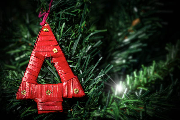 Extreme closeup of a small and red Christmas tree made of woven straw hanging on a green Christmas tree.