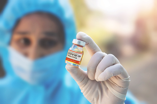 Young woman doctor in PPE protective mask and gloves holding a syringe and coronavirus vaccine. The concept of a new vaccine against the disease, flu vaccine vaccination