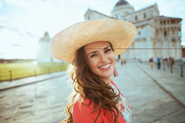 smiling trendy woman in floral dress exploring attractions smiling trendy traveller woman in floral dress with hat exploring attractions in square of miracles in Pisa, Italy. pisa leaning tower of pisa tower famous place stock pictures, royalty-free photos & images