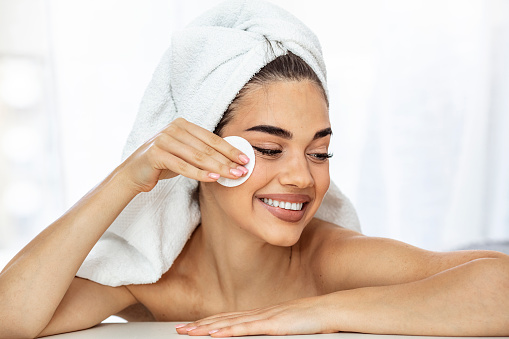 Woman using cotton pad. Happy smiling beautiful young woman cleaning skin by cotton pad. light background. Beautiful Spa Woman Smiling. Perfect Fresh Skin. Youth and Skin Care Concept