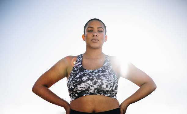 Confident plus size female model in sportswear Plus size female in sportswear standing with her hands on hips. Confident female standing outdoors with sun shining from behind. body confidence stock pictures, royalty-free photos & images