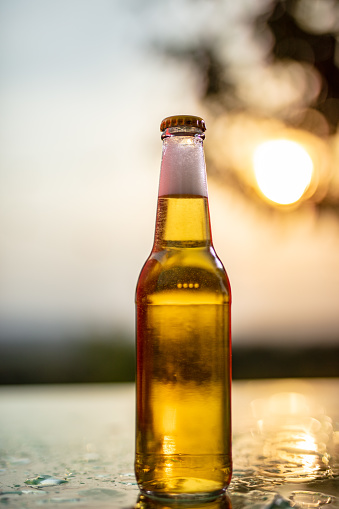 Close up two clear glass bottles of cold lager beer on ice cubes over background of summer sea and sky, low angle side view