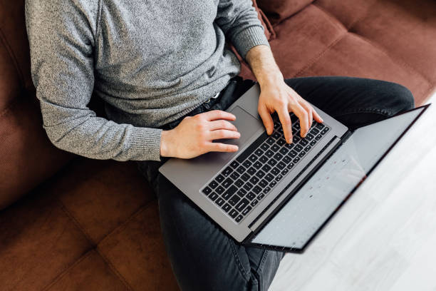 istock Handsome young man using laptop computer at home. Student man is reading the book. Online shopping, home work, freelance, online learning, studying concept. Distance education 1297395976