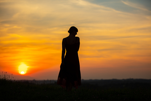 Silhouette of woman standing on grass field during sunset