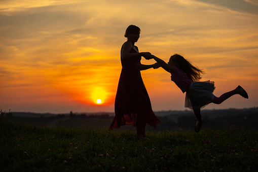 Silhouette of a playful mother lifting and spinning her daughter outside at sunset