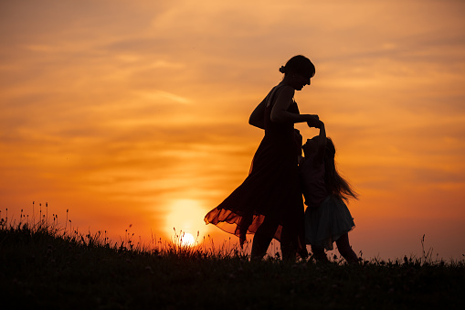 A Silhouette of mother and daughter playing outside in meadow at sunset
